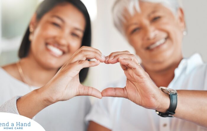 A daughter and an older mother create a heart with their hands, representing the feeling that is highlighted during National Family Caregivers Month